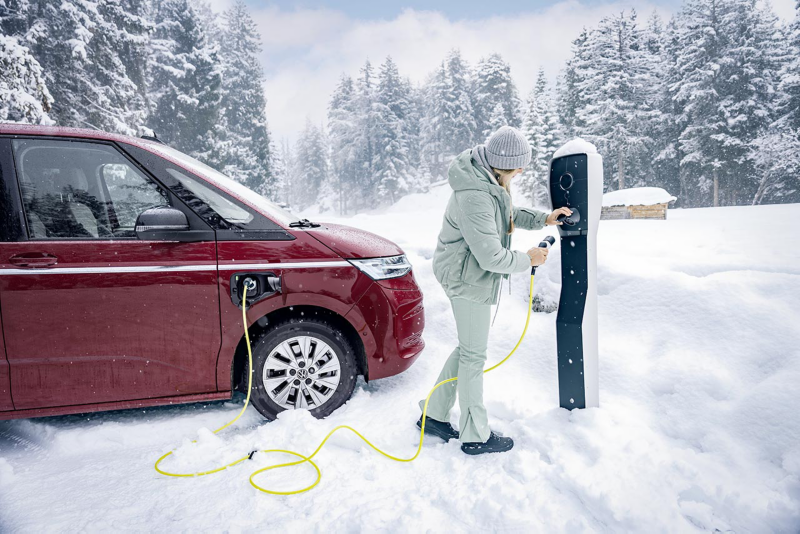 Un hombre del servicio técnico de VW sujetando el conector de carga, con un VW ID. Buzz detrás.