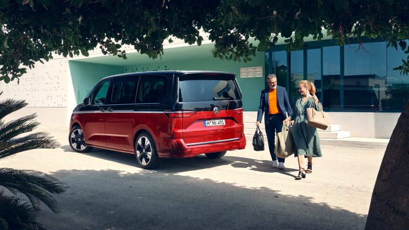 En man och kvinna går bakom sin svart-röda förmånsbil i form av en VW Multivan