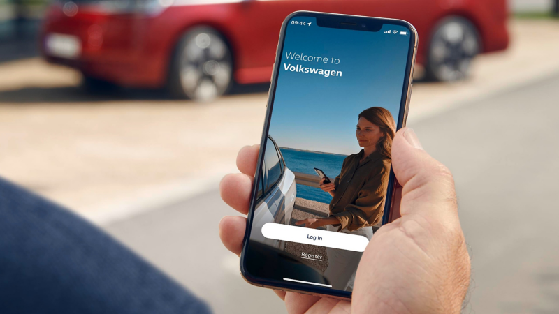 Eine Nahaufnahme zeigt eine Hand, die ein Smartphone mit der "Welcome to Volkswagen"-Anmeldeseite hält.