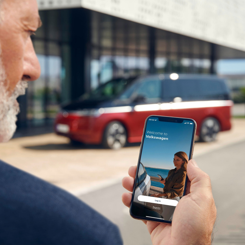 Person nutzt die Volkswagen App auf einem Smartphone vor einem Volkswagen Multivan. 