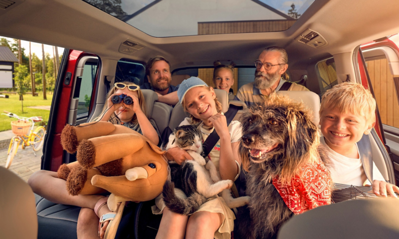 Eine Großfamilie mit Hund, Katze und Plüschtier sitzen in den hinteren zwei Sitzreihen eines VW Multivan.