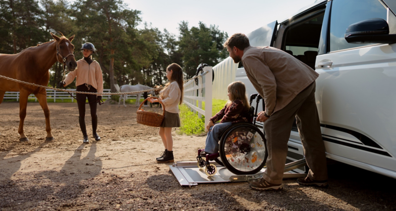 Ein Kind im Rollstuhl steigt mit einem Rollstuhllift aus einem VW Multivan.