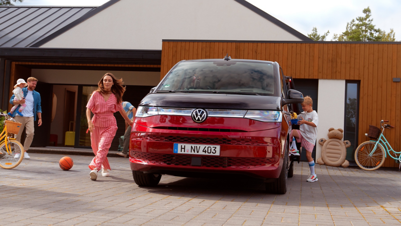 Ein VW Multivan parkt in einer Auffahrt vor einem Haus, daneben spielen Kinder einer Familie.