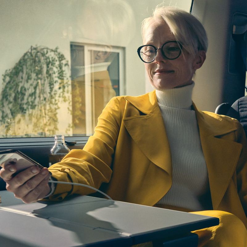 Kobieta siedzi w Volkswagenie i włącza aplikację We Connect w swoim smartfonie.