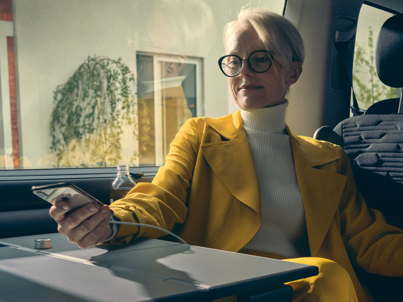 Een vrouw zit in een Volkswagen en activeert de We Connect-app op haar smartphone.