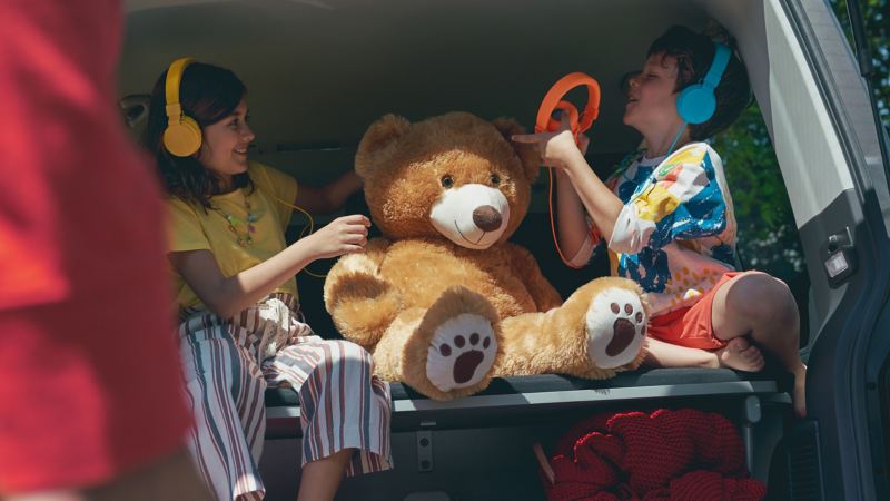 Zwei Kinder sitzen im umgebauten Kofferraum eines Volkswagen und haben Kopfhörer auf.