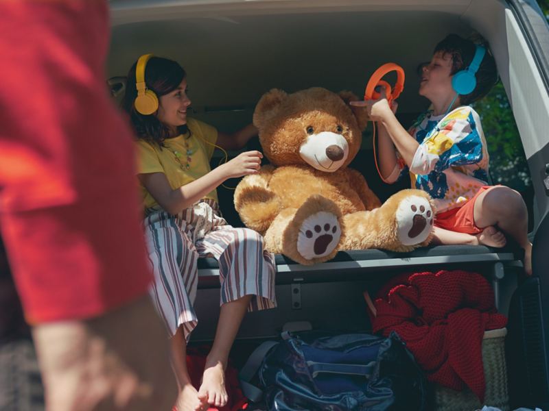 Zwei Kinder sitzen im Kofferraum eines VW Bullis.
