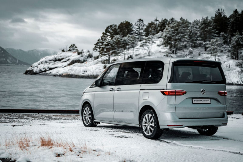 Volkswagen Multivan stoi na brzegu jeziora na tle gór w zimie.