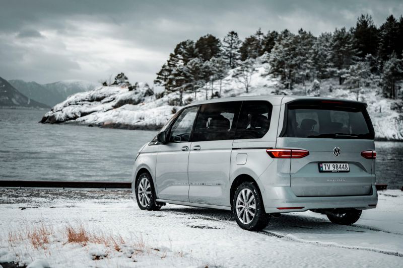 Un Volkswagen Multivan est garé devant un lac avec un paysage enneigé