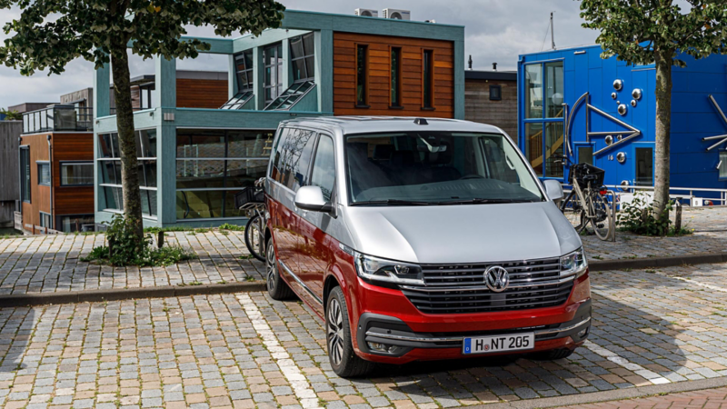 En tvåfärgad silver-röd VW Multivan T6.1 framför spännande arkitektur i Amsterdam