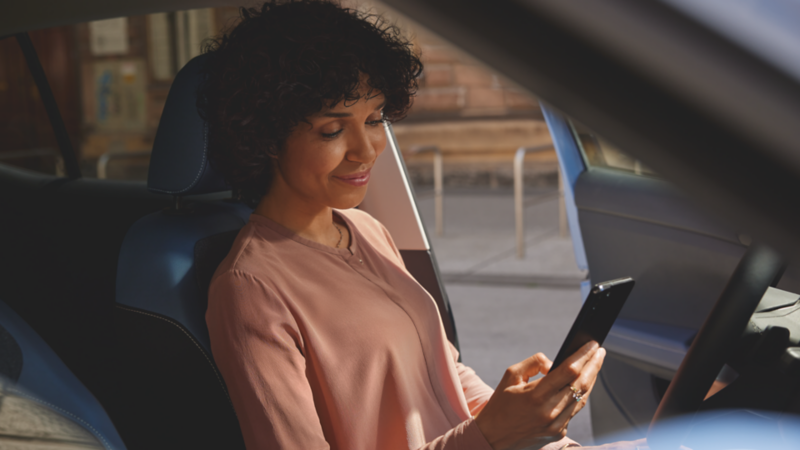 Une femme regarde un smartphone dans ses mains tout en étant assise sur le siège conducteur d'une voiture.