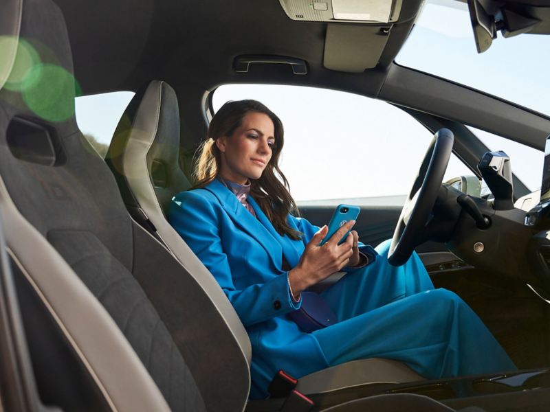 Een vrouw zit in een Volkswagen en kijkt op haar mobiele telefoon