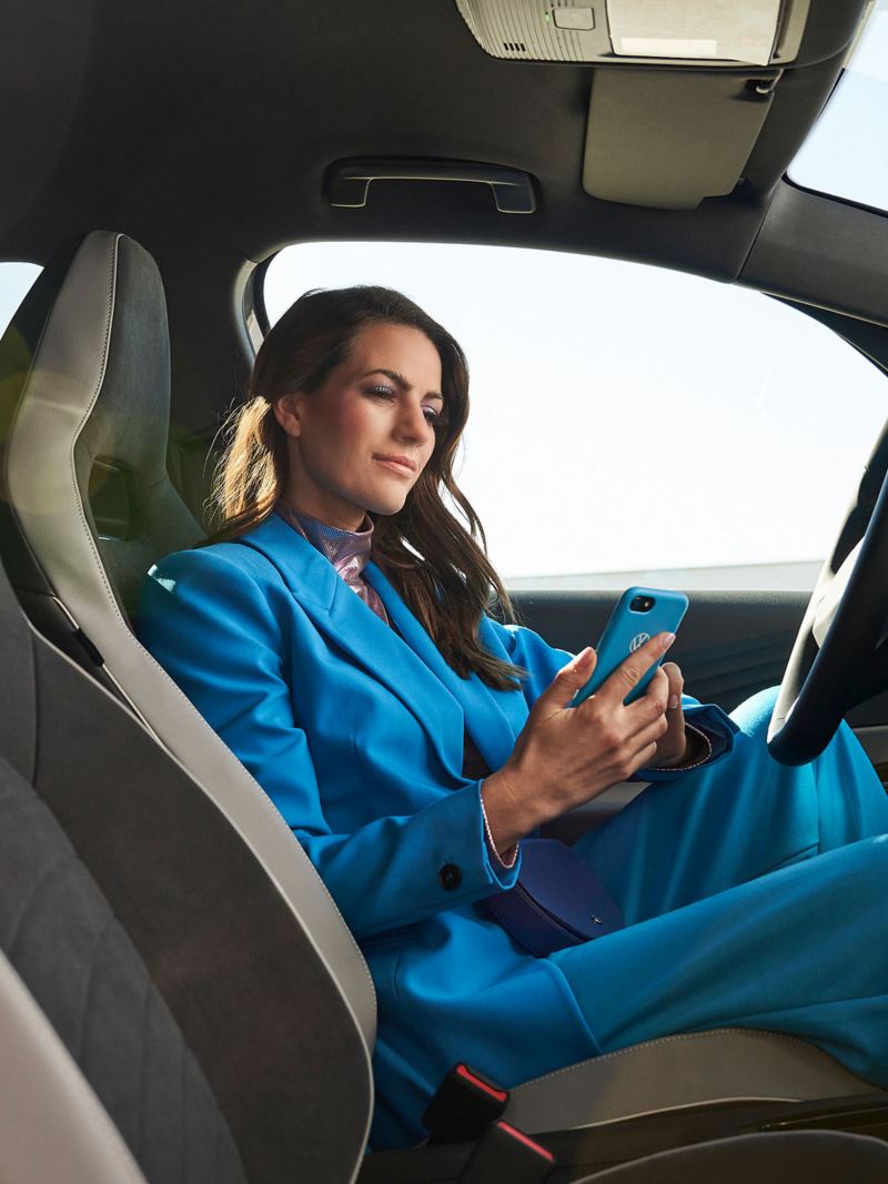 Μια γυναίκα κάθεται σε ένα όχημα Volkswagen και κοιτάζει το κινητό τηλέφωνό της