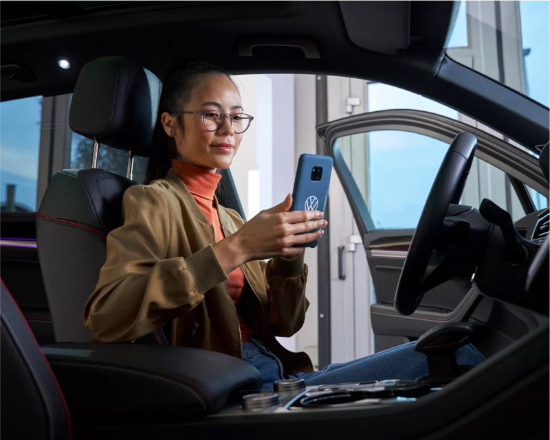 Woman using myVW app on mobile phone in Volkswagen vehicle.