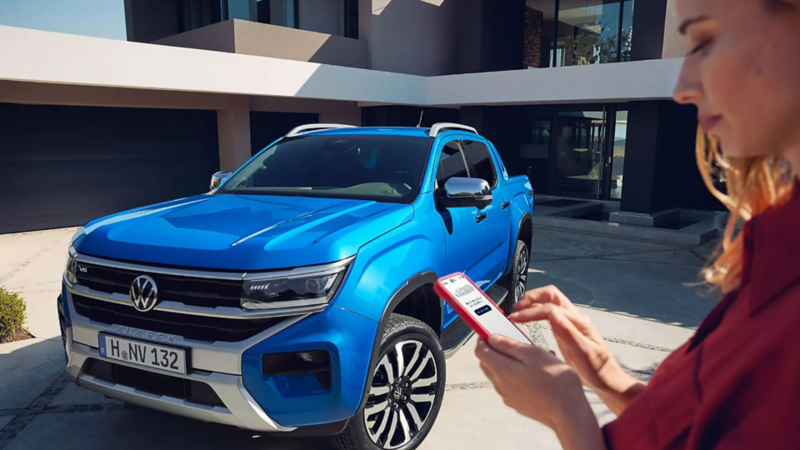 Una donna guarda lo smartphone vicino a Volkswagen Nuovo Amarok.