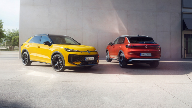 Ein gelber VW T-Roc R-Line und ein roter VW T-Roc Style stehen nebeneinander vor einem modernen Gebäude.