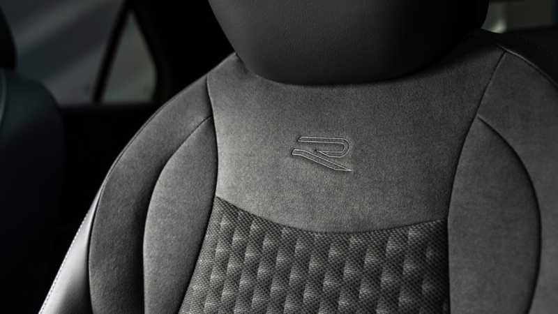 Detailaufnahme einer schwarzen Sitzlehne im VW T-Roc, mit eingeprägtem „R“-Logo und strukturierter Polsterung.