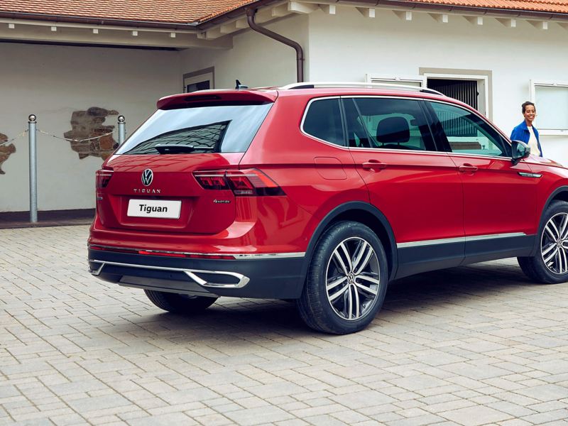 A red Tiguan Allspace Elegance stands in an equestrian yard, the rear with VW logo at a distance from a flower pot.