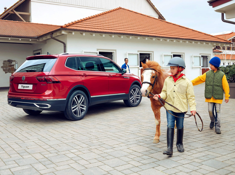 A man leans against the hood of a white Tiguan Allspace R-Line, the LED matrix headlights and light bar on. 