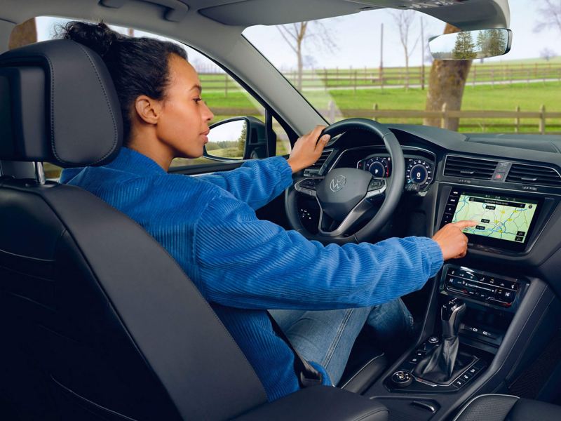 A woman sits in the driver's seat with optional seat climate control of the Tiguan Allspace Elegance and operates the display. 