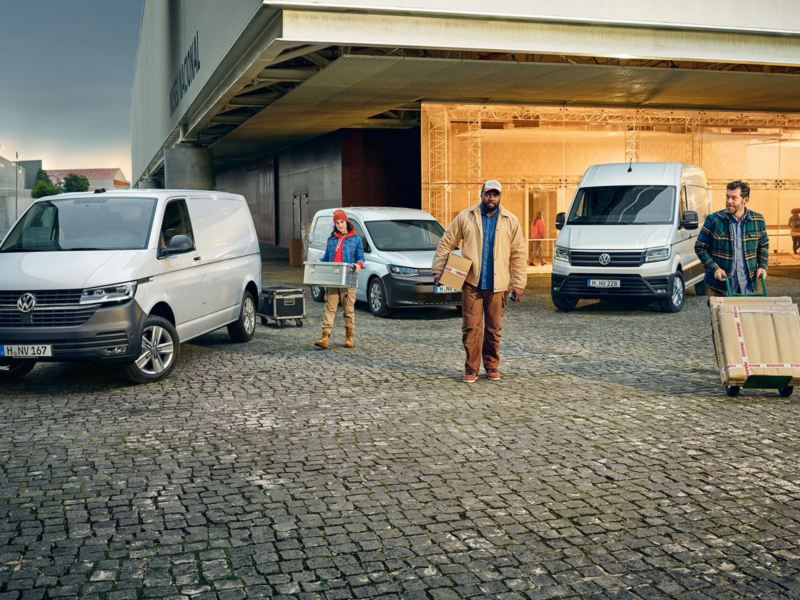 Enkele Volkswagen bedrijfsvoertuigen voor een gebouw, met daarvoor 3 mensen