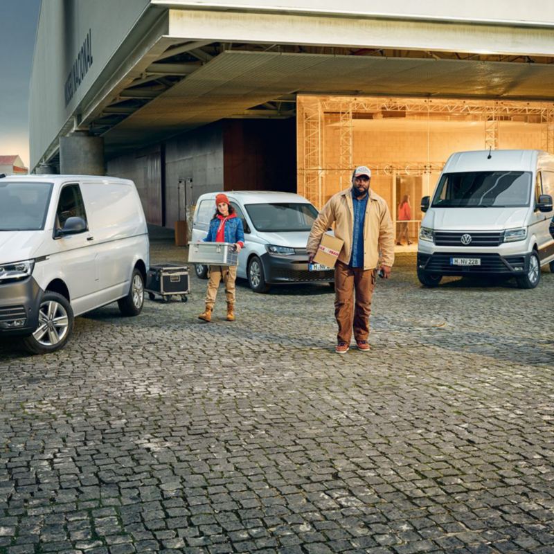 Enkele Volkswagen bedrijfsvoertuigen voor een gebouw, met daarvoor 3 mensen