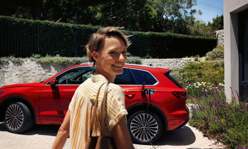 A woman walking towards her parked red Volkswagen Touareg on a driveway