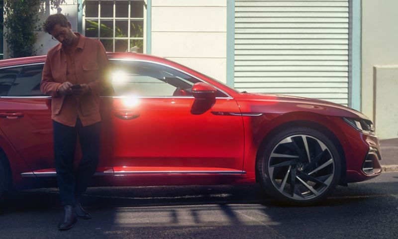 A man leaning against a red Arteon Shooting Brake car