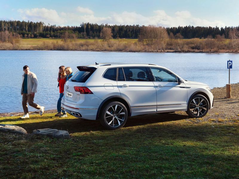 A white Tiguan Allspace R-Line with tinted rear windows parked next to a lake