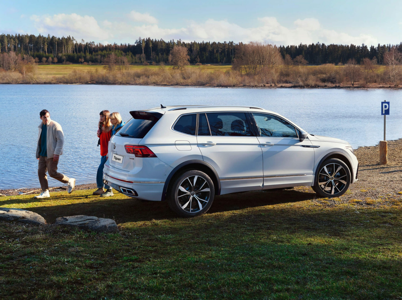 A white Tiguan Allspace R-Line with tinted rear windows parked next to a lake