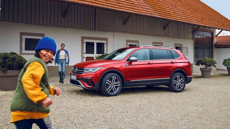 Photo of a red Tiguan Allspace parked in front of a house with a family stood next to it. 