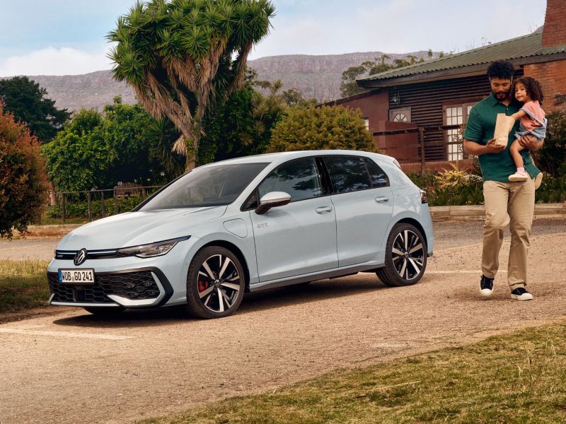 A parent holds their child as they walk away from a Golf GTE