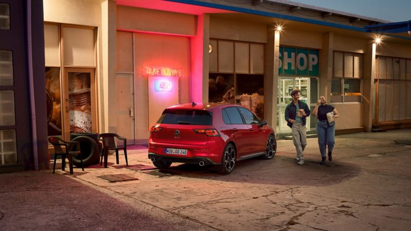 Red Golf GTI parked sideways in front of a shop, two people walking past