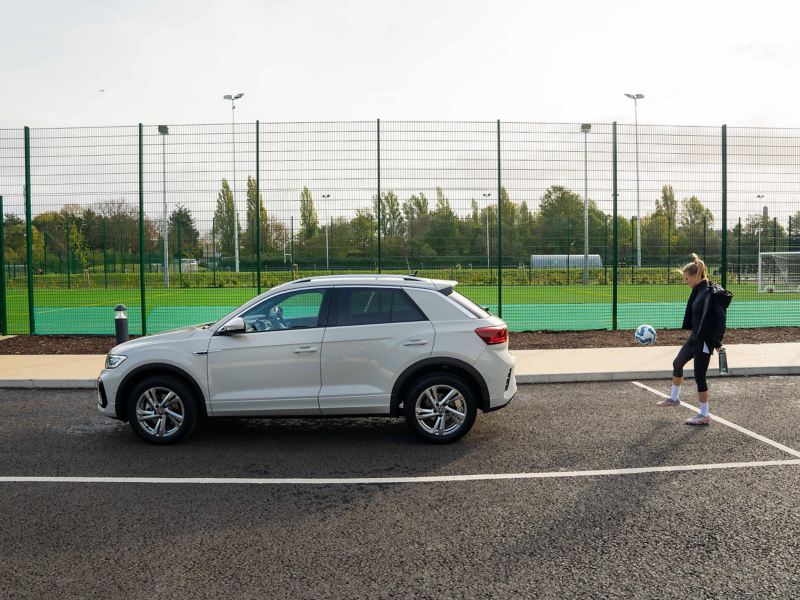 A yound lady doing keep ups with a football by the side of a parked T-Roc