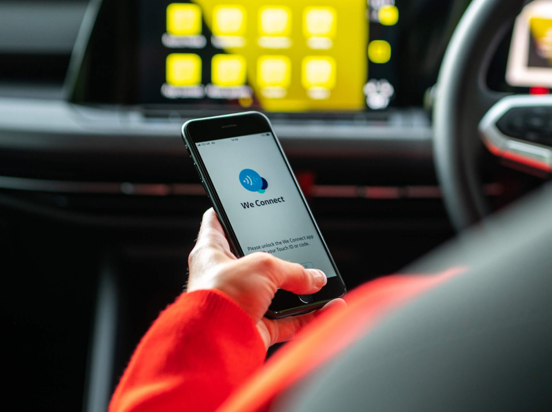The woman using a phone while standing on the street in front of a yellow Golf 8