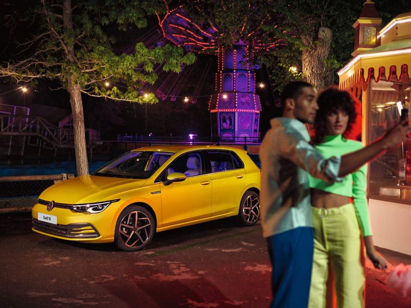 A couple talking at a fair with a yellow Golf 8 in the background.