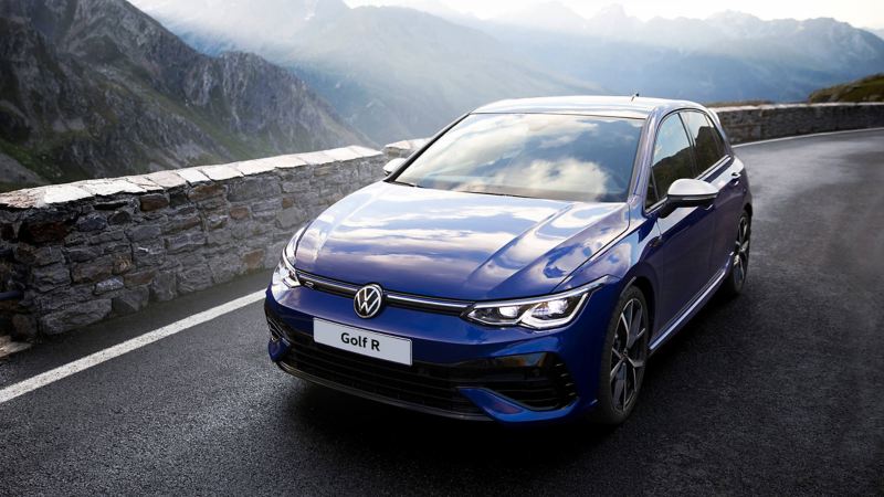 The new Golf R drives on the edge of a mountain road. Mountains are in the background.
