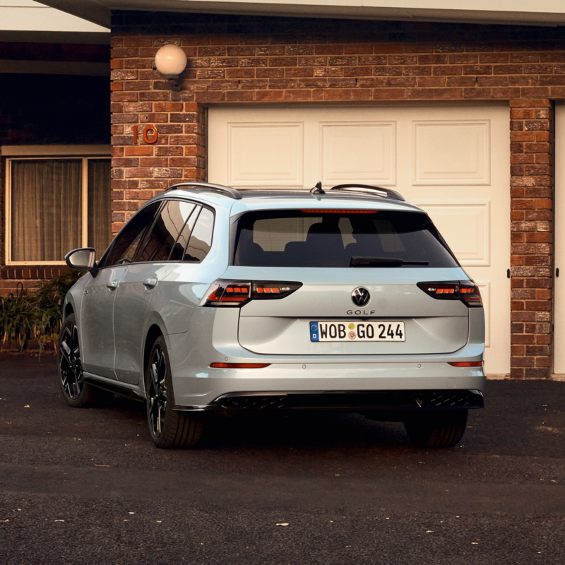 A young woman is standing behind a white VW Golf Estate using her smartphone.