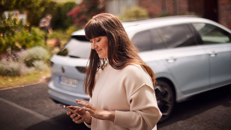 A Golf Estate parked on a drive with a lady standing next to it looking at her smartphone