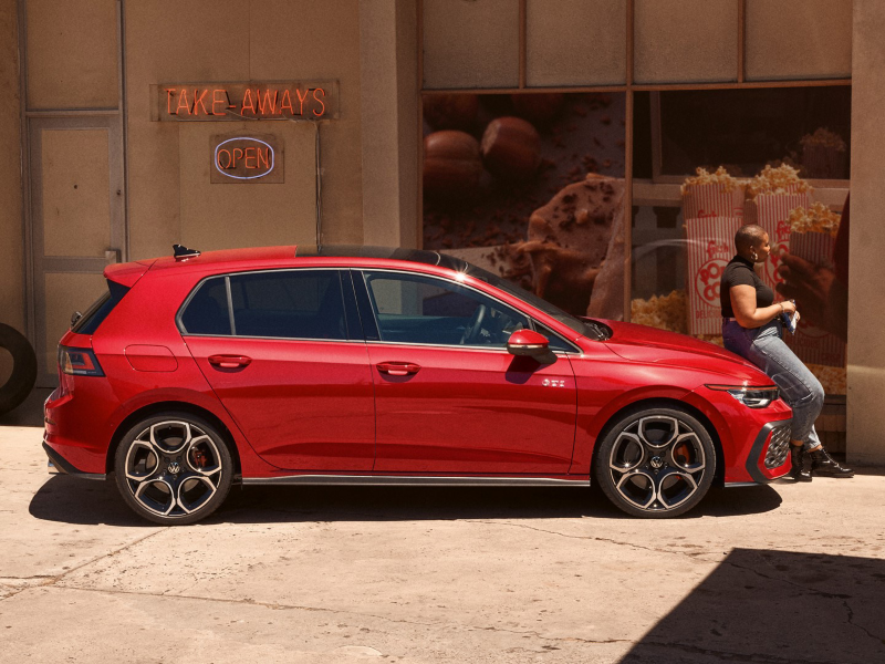 A red VW Polo GTI parked outside a shopfront with a person sitting on the bonnet