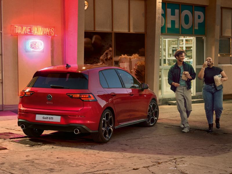 A red VW Polo GTI parked outside a shopfront as two people approach