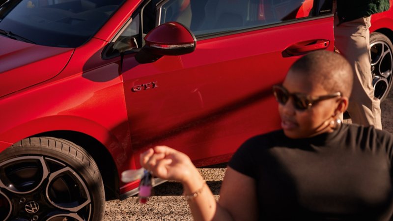 Person sitting next to a red Golf GTI holding their keys