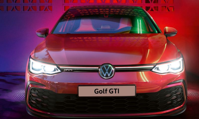 A red VW Golf 8 GTI with headlights on