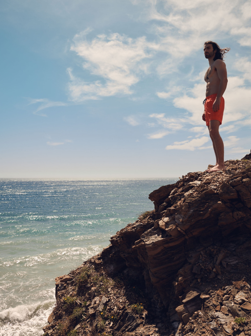 A man stands on a rock and looks out to sea