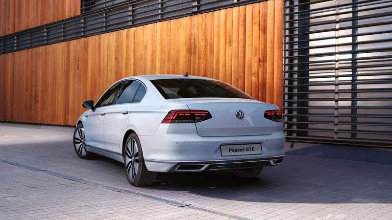 A rear shot of a white Volkswagen Passat GTE parked outside a building.