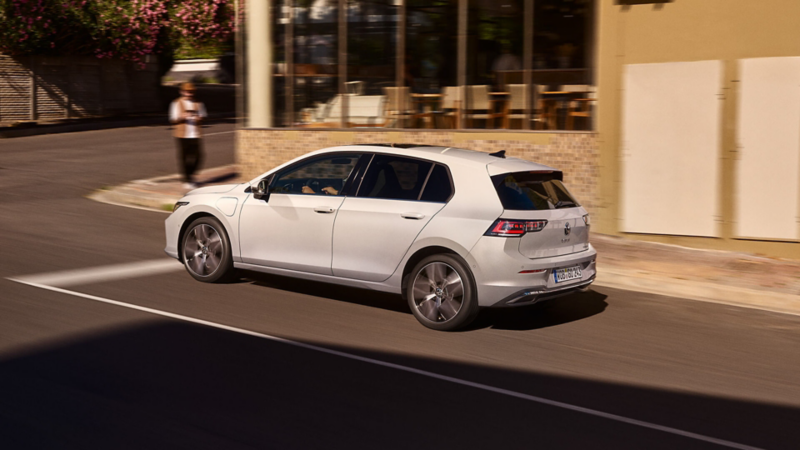 A white Golf eHybrid driving past a café