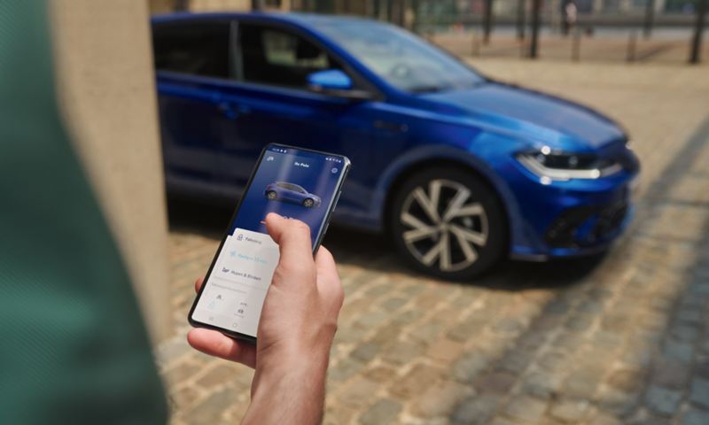 View of a mobile phone display with vehicle data of the Polo, in the background the VW Polo in blue, parked.