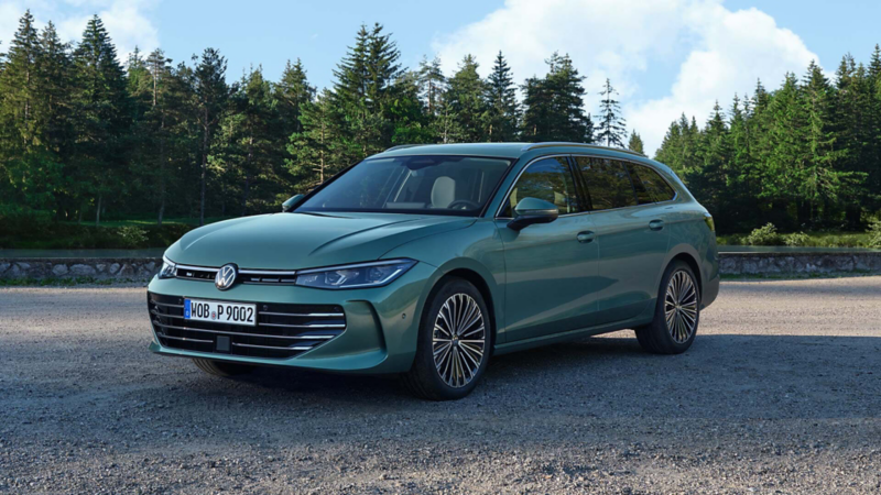 Bluish green VW Passat standing on a gravel surface, the area borders on a pine forest.