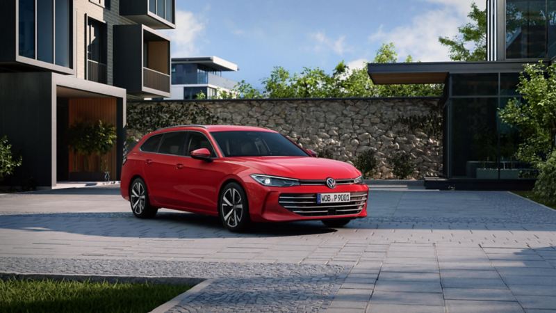 A red Passat stands in the courtyard of a modern residential complex in lateral perspective and with the front facing the viewer.