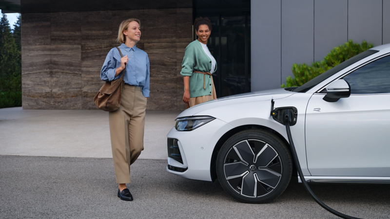 Two women walking past a Volkswagen Passat that's being charged